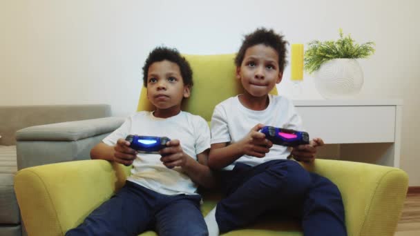 Zwei kleine schwarze Jungen Brüder spielen Spiel und ihre Eltern bringen ihre Hausaufgaben statt Joysticks — Stockvideo