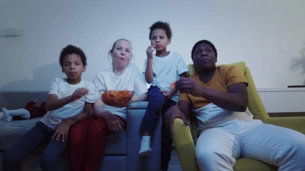Multirace familj tittar på TV och äter chips på kvällen — Stockvideo