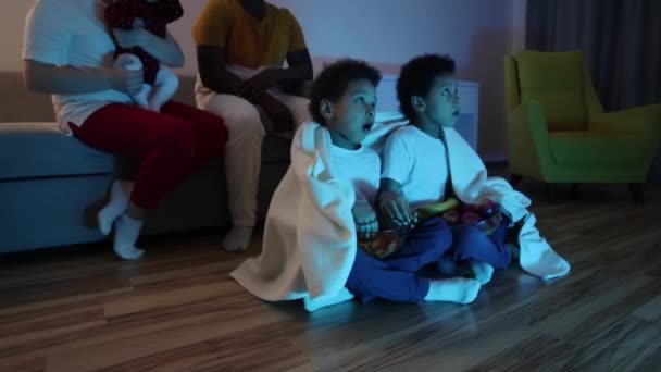 Мультикультурная семья смотрит телевизор и братья-близнецы едят фрукты — стоковое видео