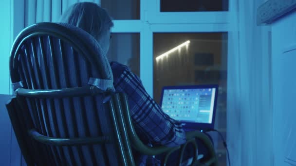 Fiatal szőke férfi ül egy hintaszékben és laptopot használ — Stock videók