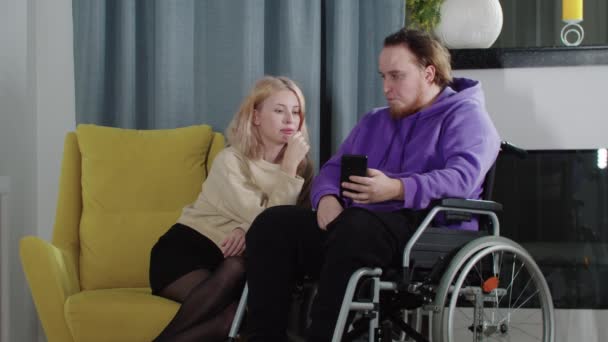 Szczęśliwa para blondynka i mężczyzna na wózku inwalidzkim patrząc na ekran telefonu i przewijania zdjęć — Wideo stockowe