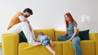 Aile sarı koltukta oturuyor ve bebek kanepeden iniyor.