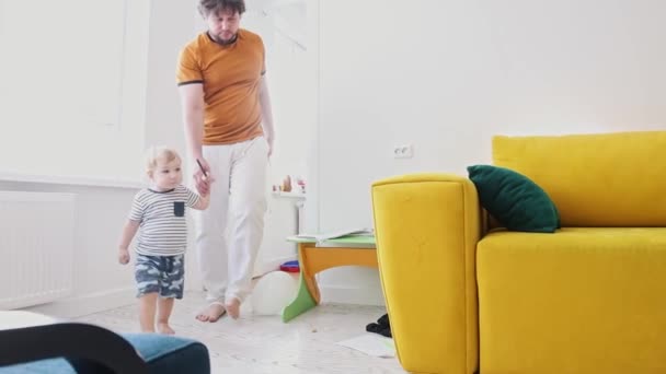 Seorang ayah membawa anaknya ke ruang tamu dan dia duduk untuk melukis dengan krayon terang — Stok Video