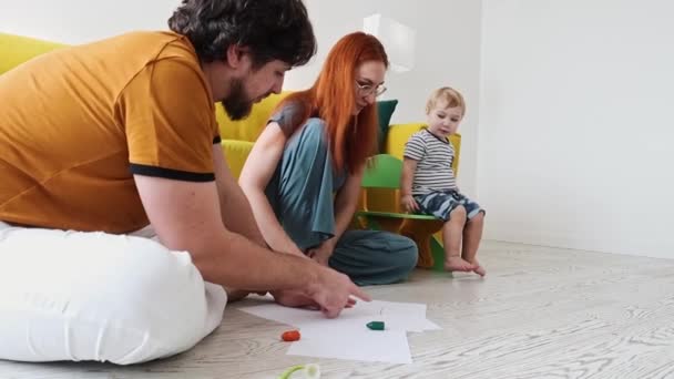 床に座り、紙の上にカラフルなクレヨンで絵を描く家族 — ストック動画