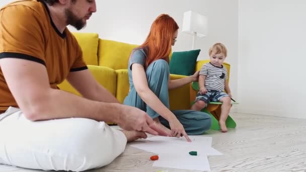 床に座っている家族と紙の上にカラフルなクレヨンでお父さんの絵 — ストック動画