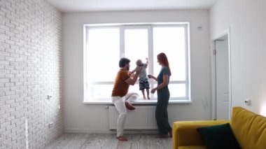 Mutlu bir aile, küçük oğluyla pencerenin önündeki beyaz salonda oynuyor.