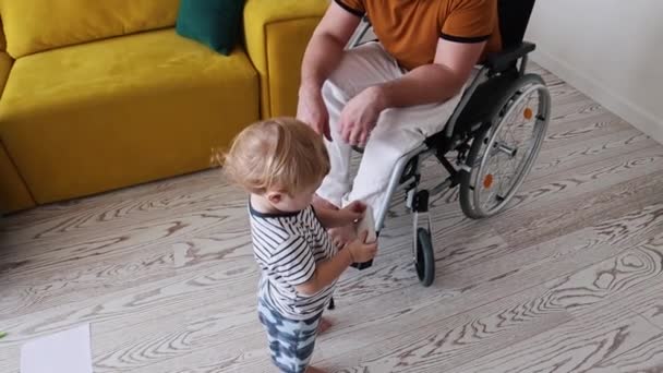 Mały chłopiec montuje pilota z telewizora - spaceruje od ojca na wózku inwalidzkim do matki — Wideo stockowe