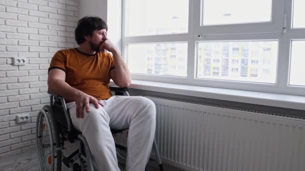 Vuxen ledsen man i rullstol sitter nära fönstret — Stockvideo