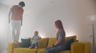 Sarı koltukta oturan aile. Babası kolluk takıp bebeğini izliyor.