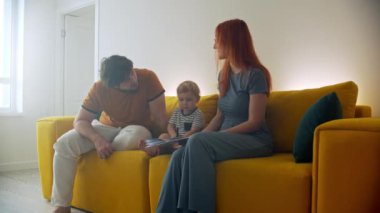 Aile sarı koltukta oturuyor ve bebek kitaba bir şeyler çiziyor.