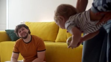 Anne bebeği sallıyor ve onu gülümseyen babaya veriyor.