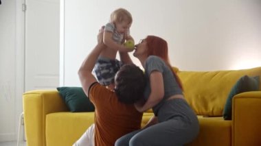 Mutlu bir aile yerde oturup bebekle oynuyor.