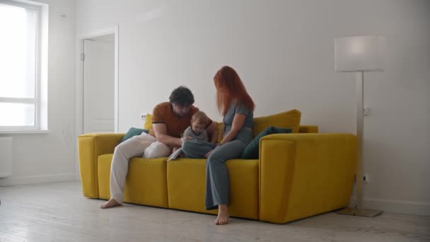 Familie sitzt auf gelbem Sofa und Eltern bringen ihrem Baby das Schreiben bei — Stockvideo