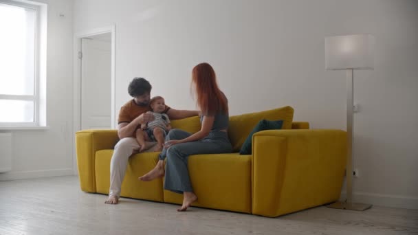 Família sentada no sofá amarelo e o bebê segurando dois lápis — Vídeo de Stock