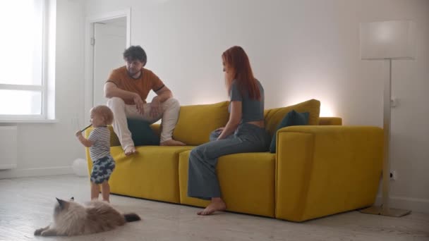 Familie sitzt auf gelbem Sofa und das Baby geht weg - sein Vater beobachtet ihn — Stockvideo
