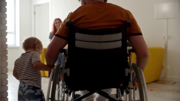Ett litet barn hjälper sin far att åka rullstol — Stockvideo