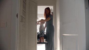 Küçük bir bebek sandalyenin üzerinde durur ve annesi dolabı açar.