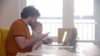 Yalnız baba dizlerinin üzerinde bebeğiyle bilgisayarı kullanarak çalışmaya çalışıyor.