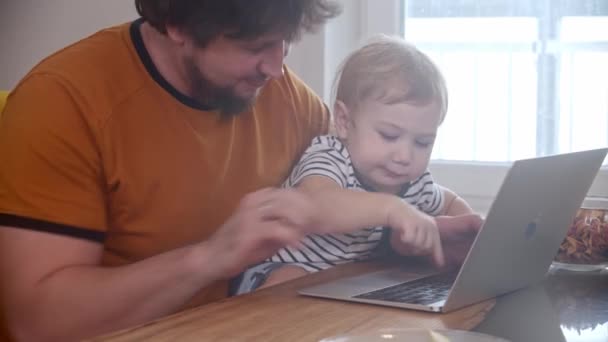 Yalnız babası dizüstü bilgisayarıyla çalışıyor ve küçük bebeği dizlerinin üstüne çöküp düğmelere basıyor. — Stok video