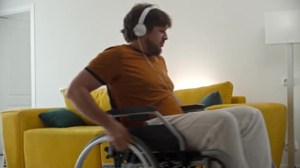 Man i rullstol i hörlurar lyssnar musik och rullar runt i rummet — Stockvideo
