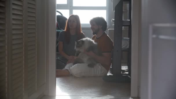 Feliz familia sentado en el suelo y su mullido gato viene a ellos — Vídeo de stock