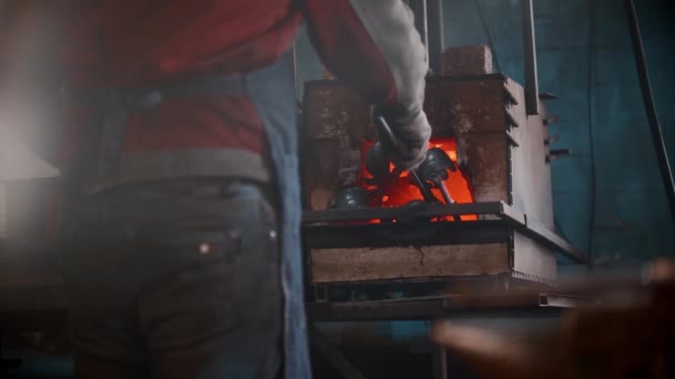 Smid workshop - een man zet metalen ding in de oven met een tang — Stockvideo
