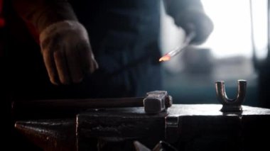 Demirci atölyesi. Bir adam ısıtılmış bir metal parçasına çekiçle vuruyor.