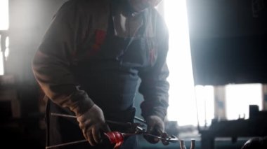 Demirci atölyesi. Bir adam forseps kullanarak hararetli detaylarla çalışır.