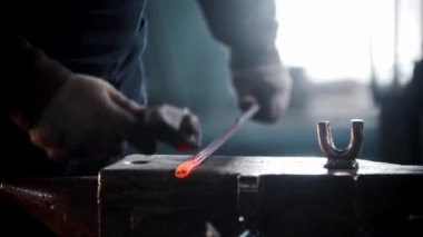 Demirci atölyesi. Bir adam ısıtılmış bir metal parçasına çekiçle vurup büker.