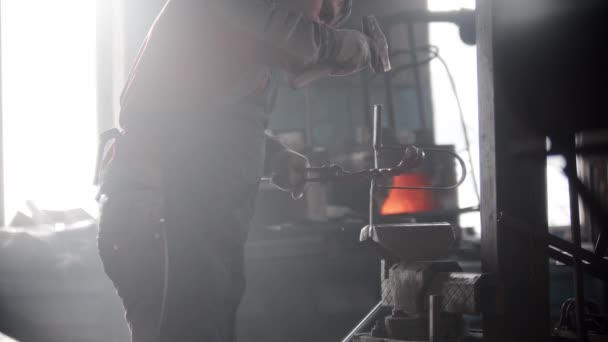 Schmiedewerkstatt - ein Mann arbeitet mit einem erhitzten Metallteil in der Pressbinde - schlägt mit einem Hammer zu — Stockvideo