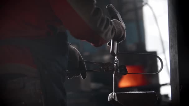 Blacksmith workshop - a man puts metal detail in the pressing retainer and hits it with a hammer making a shape and design — ストック動画