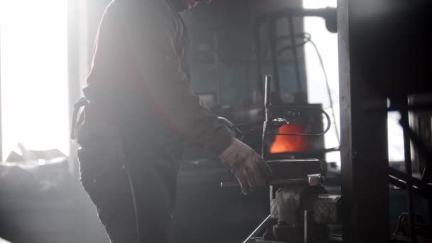 Smid workshop - een man zet metalen detail in de persbeugel en slaat het met een hamer — Stockvideo