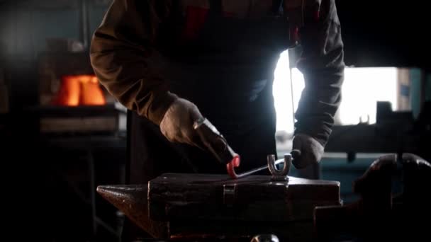 Oficina de ferreiro - um homem dobra um pedaço de metal com um martelo na bigorna — Vídeo de Stock