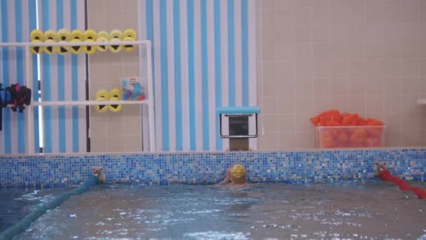 一个头戴黄帽的游泳者抓住游泳池边的看台把手 — 图库视频影像