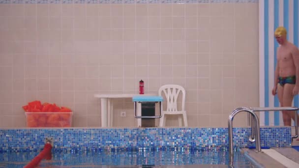 Fit man swimmer jde ke stojanu u bazénu a postaví se na něj — Stock video