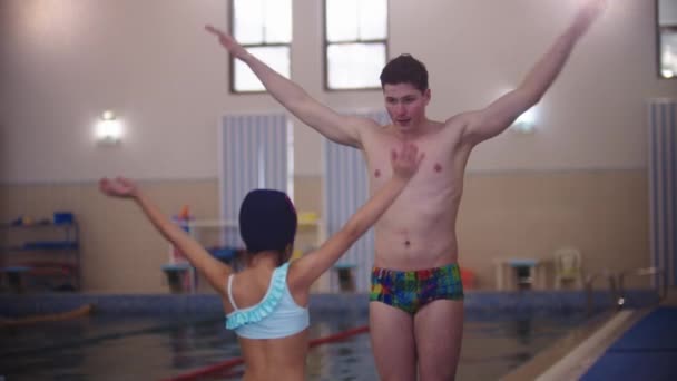 Instructor de natación calentando sus hombros con una niña en la piscina — Vídeo de stock