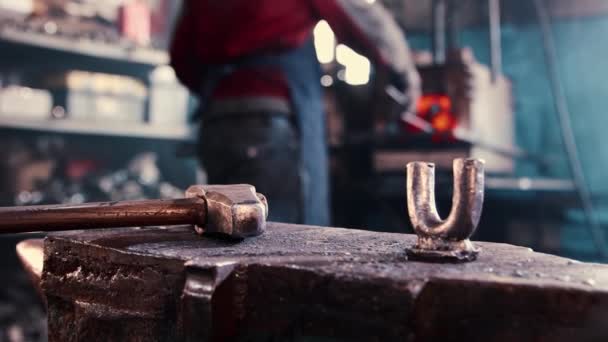 Anvil and hammer on the foreground and man blacksmith working in the background — Stock Video