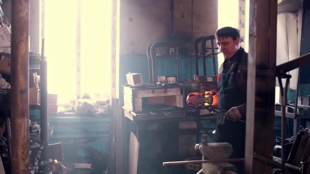 Homem ferreiro tira uma peça de metal de um forno e olha para a câmera — Vídeo de Stock