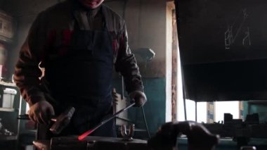 Demirci dikdörtgen bir metal parçası çıkarır ve örse çekiçle vurmaya başlar.