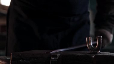 Demirci çekiçle dikdörtgen metal bir parçaya vuruyor.