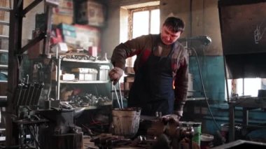 Demirci adam, bir kova suda ısıtılmış kırmızı metali soğutuyor.