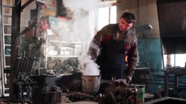 Demirci adam bir kova suda metal parçaları soğutuyor.