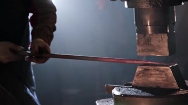 Demirci adam, otomatik makinenin altında kızgın bir metal parçasını inceliyor.