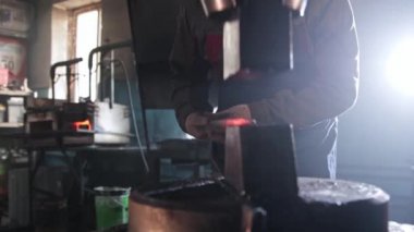Demirci, otomatik bir basın makinesinin altında kızgın bir metal parçasını inceliyor.