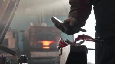 Demirci ince bir metal parçasını örs ve çekiçle şekillendiriyor.