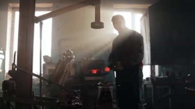 Demirci adam sıcak metal parçasını örsün üzerinde bir form kullanarak şekillendiriyor ve bir basın mensubuyla detaylara vuruyor.