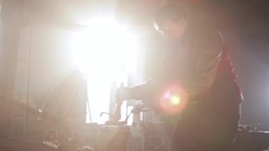 Demirci adam sıcak bir metal parçasını örsün üzerinde bir form kullanarak büküyor ve basına vuruyor.