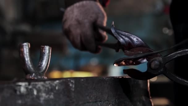 대장장이는 겸자를 사용하여 기다란 금속 조각을 구부리고 있다 — 비디오