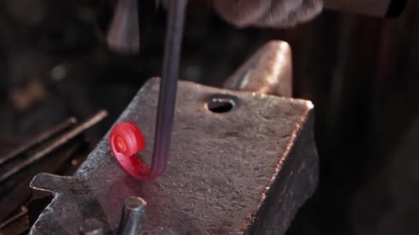 Ferreiro dobra em uma espiral um detalhe de metal aquecido vermelho oblongo batendo com um martelo — Vídeo de Stock