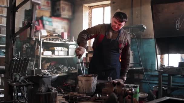 Man blacksmith cooling down red heated metal detail in a bucket of water — Stock Video